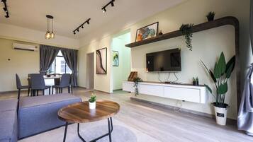 Un salon moderne comprenant un coin repas, un téléviseur à écran plat fixé sur une console blanche et une grande plante en pot.