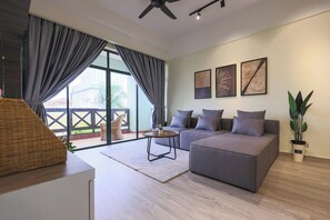 Un salon moderne avec un canapé gris, une table basse ronde et un ventilateur de plafond. Trois œuvres d’art sont accrochées au mur, et une plante en pot est posée sur le sol.