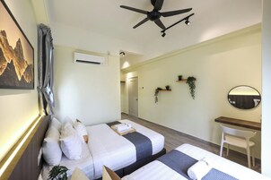 Habitación de hotel con dos camas, ventilador de techo, unidad de aire acondicionado, escritorio con silla y estantes en la pared con plantas.