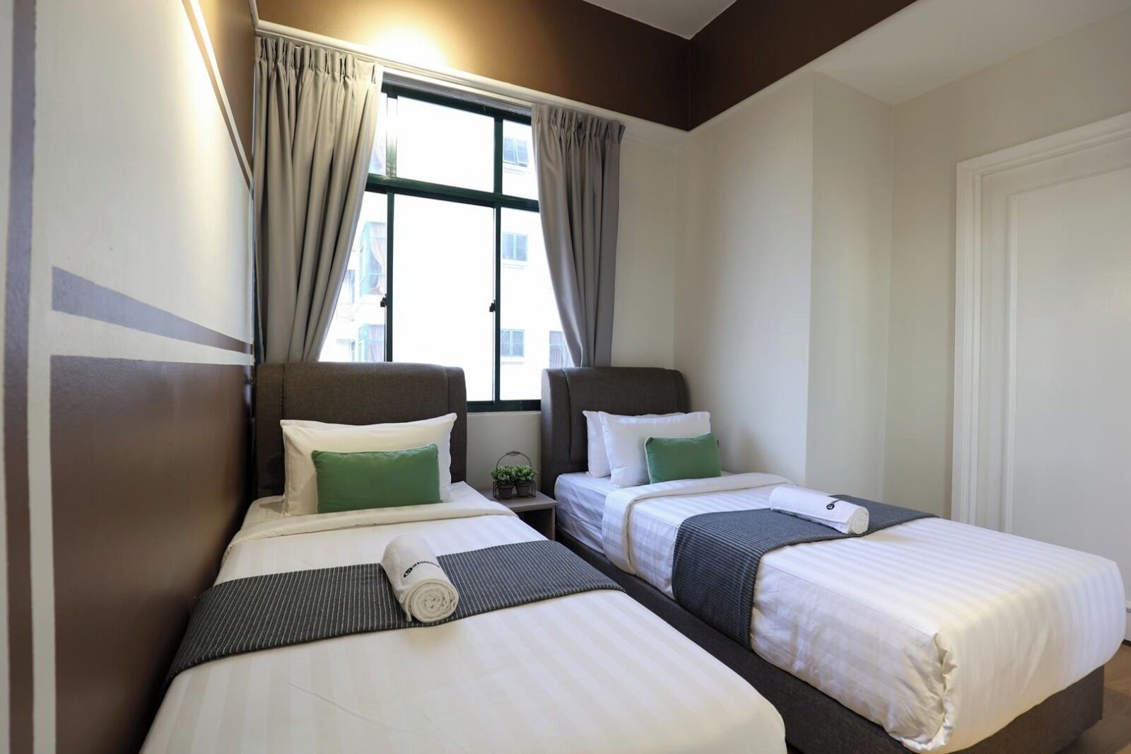 A hotel room with two single beds, a window with curtains, and a door.