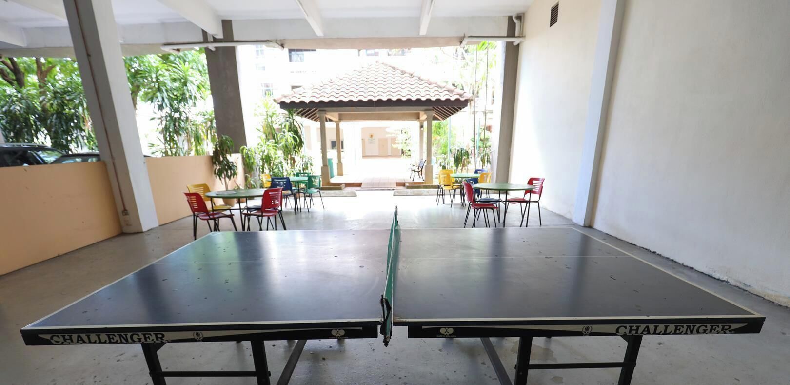 A ping pong table with 'CHALLENGER' branding, surrounded by chairs and tables in a covered outdoor area.
