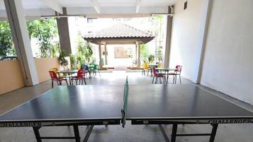 Una mesa de ping pong con la marca 'CHALLENGER', rodeada de sillas y mesas en un espacio cubierto al aire libre.