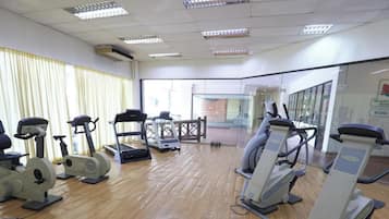 Ein Fitnessstudio mit verschiedenen Trainingsgeräten, Holzboden und Blick nach draußen durch große Fenster.