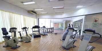 Un gimnasio con distintas máquinas de ejercicio, suelo de madera y vistas al exterior a través de amplias ventanas.
