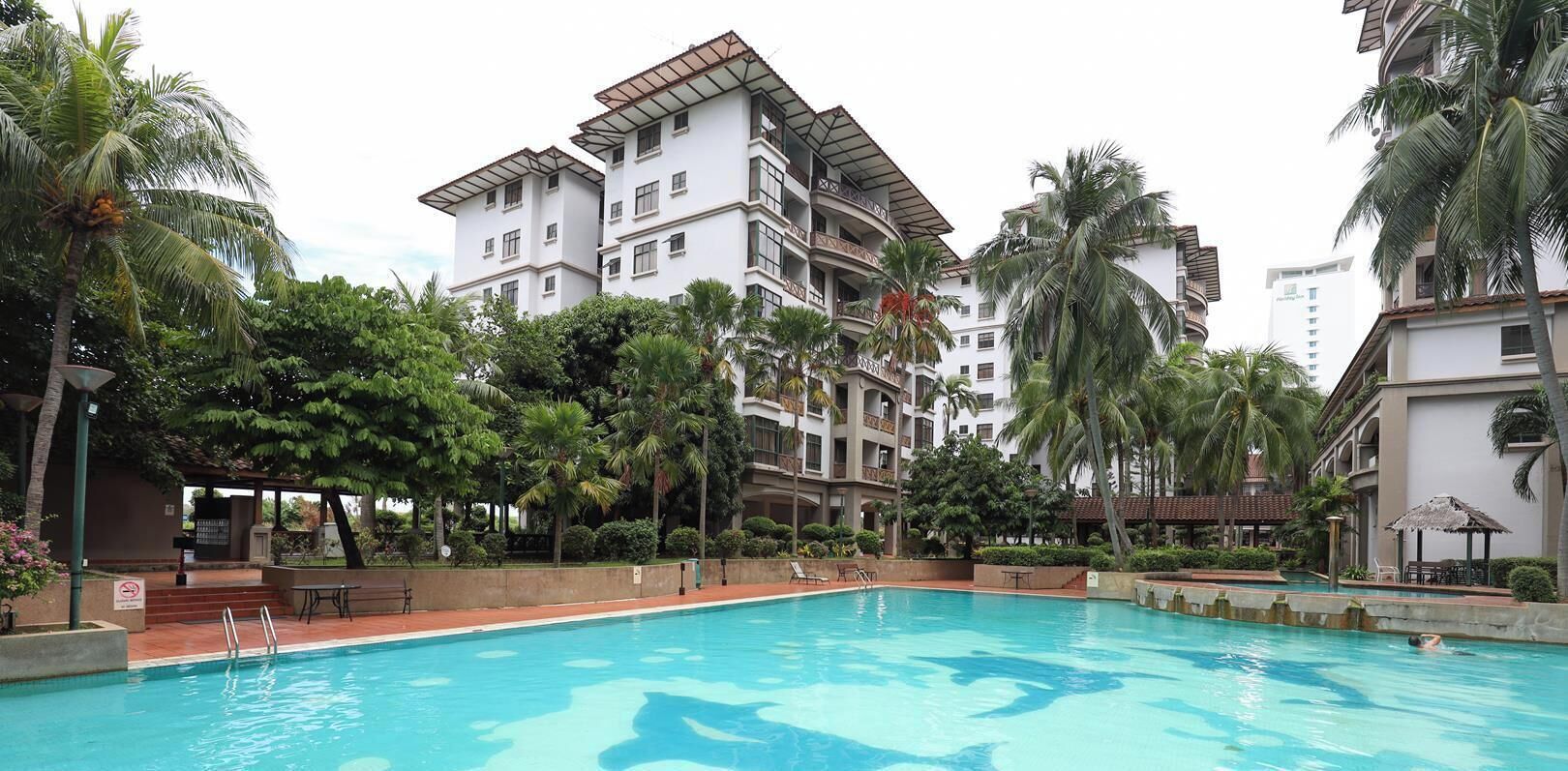 Piscina rodeada por palmeiras e um edifício com várias andares e varandas.