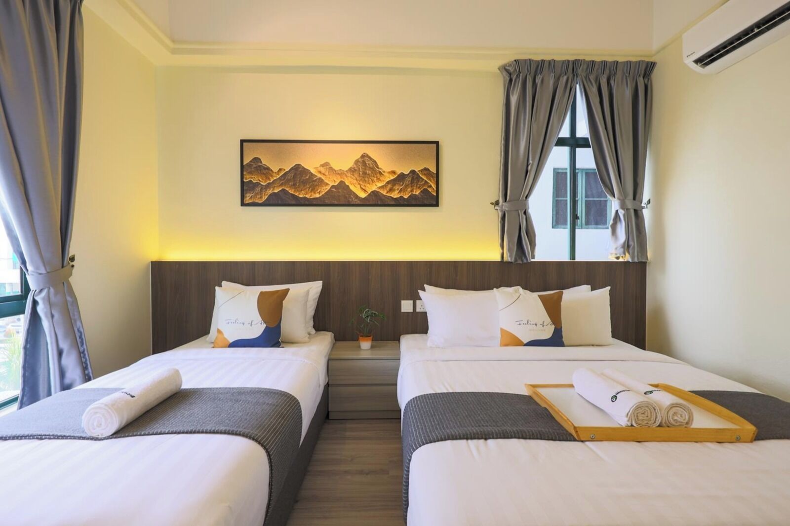 Habitación de hotel con dos camas, un cuadro de montañas, una ventana con cortinas y un equipo de aire acondicionado.
