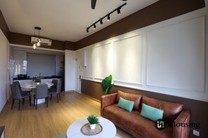 A modern living room with a brown leather sofa, a dining table with chairs, and a kitchen in the background. - Mahkota Jonker Melaka By I Housing (Malacca City)