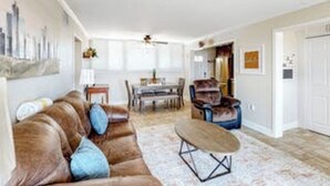 Een woonkamer met een bruine leren bank, een houten salontafel, en een eethoek met een tafel en stoelen.