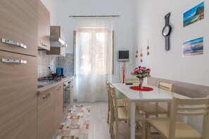 A modern kitchen with wooden cabinets, a dining table with chairs, a TV, and a clock on the wall. - Apartment "Sicania" with Balcony, A/C & Wi-Fi (Noto)