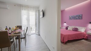 Een kamer met een bed, een eettafel met stoelen, een televisie en een raam met gordijnen.