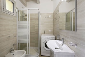 A modern bathroom with a glass shower enclosure, a built-in washing machine, and a sink with a mirror.