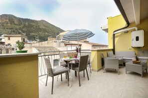 Un balcon agrémenté de meubles en osier, d’un parasol à rayures et offrant une vue sur une montagne.