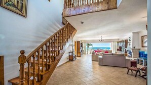 A spacious living area with a wooden staircase, a large sofa, and a view of the ocean. - Villa Oceano with Sea View, Pool, Garden & Wi-Fi (São Rafael)