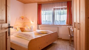 A wooden-framed room with a bed, a window with curtains, a radiator, and a chair. - Apartment 'Gamperhof Latemar' with Mountain View, Shared Terrace and Whirlpool (Karneid/Gummer)