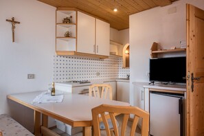 Eine kleine Küche mit Holzsäulen, einem Esstisch, Stühlen, einem Fernseher und einem kleinen Kühlschrank.