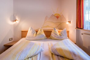 Ein Bett mit gestreifter Bettwäsche, eine Wandleuchte und ein Bergmotiv darüber.