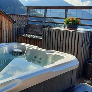 Una vasca idromassaggio su un balcone con recinzione in legno, una panca e una pianta in vaso.