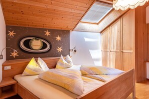 A wooden ceiling with a skylight, a bed with striped bedding, and a wall with a circular window and star decorations.