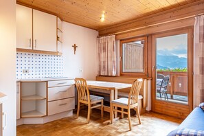 Una camera accogliente con soffitto in legno, un tavolo da pranzo con sedie, una panca, una finestra con tende e vista sulle montagne.