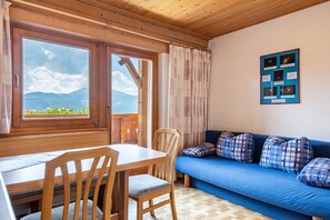 Un intérieur en bois comprenant une table à manger, des chaises, un canapé bleu et une fenêtre donnant sur les montagnes.