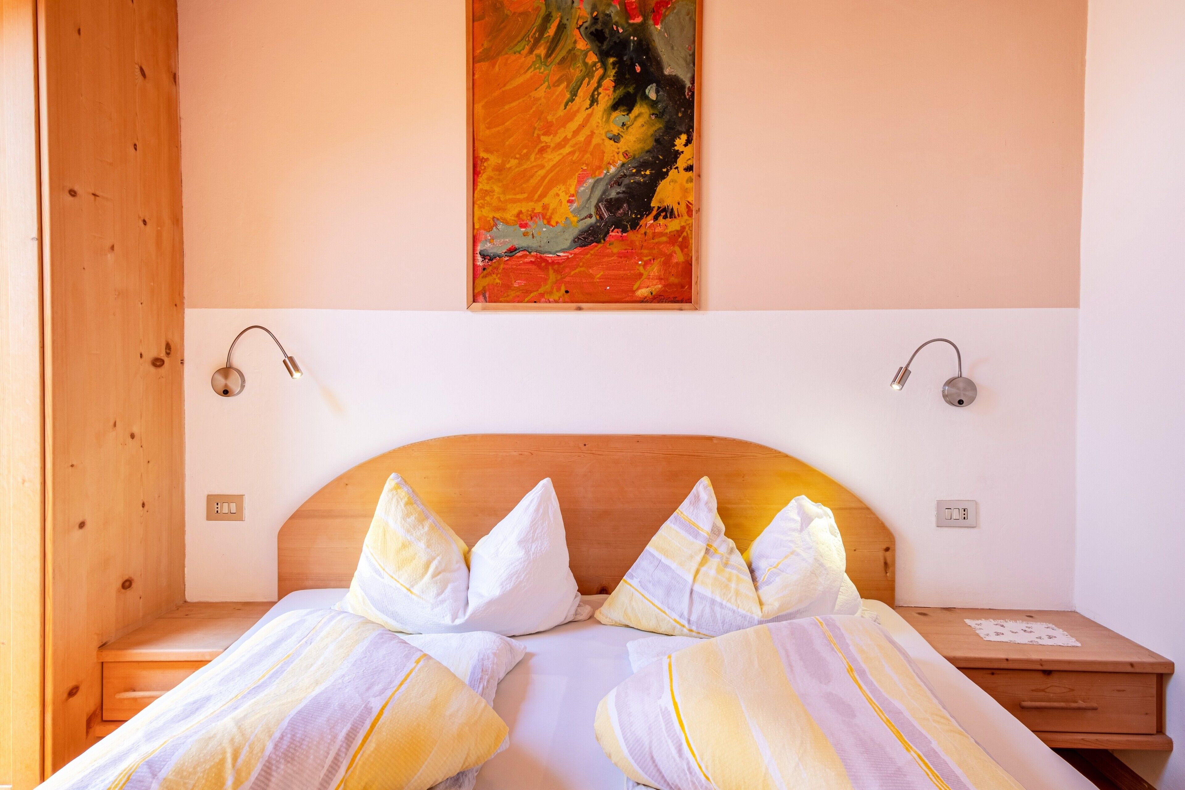 Ein Schlafzimmer mit Holz-Kopfteil, zwei Nachttischen, einem Bild an der Wand und einem Bett mit gestreifter Bettwäsche.