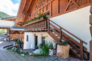 A wooden building with a balcony, a staircase, and a paved area with plants. - Apartment 'Gamperhof Planet' with Mountain View, Shared Garden and Whirlpool (Karneid)