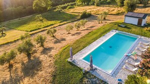Une piscine avec des chaises longues et un petit bâtiment, le tout entouré d’un paysage verdoyant et d’arbres.