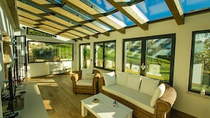 Une pièce lumineuse, baignée de soleil, avec de grandes fenêtres, des meubles en osier et un plancher en bois.
