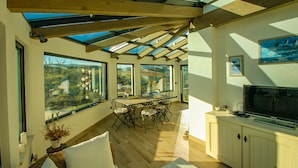 Une pièce spacieuse avec une grande table à manger, plusieurs chaises, un téléviseur et une vue dégagée grâce à de grandes fenêtres.