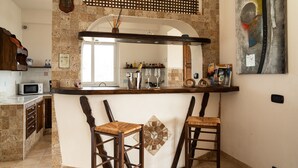 A kitchen with a stone backsplash, a bar area with stools, and a microwave. - Villa "Nel Verde" dell'Etna with Sea View, Pool, Wi-Fi, Terrace and Garden (piedimonte etneo)