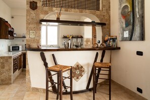 A kitchen with a stone backsplash, a bar area with stools, and a microwave. - Villa "In the Green" of Etna with Sea View, Pool, Wi-Fi, Terrace & Garden (piedimonte etneo)