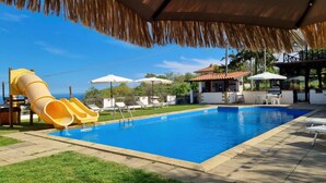 A swimming pool with a slide, lounge chairs, umbrellas, and a bar area. - Villa "Nel Verde" dell'Etna with Sea View, Pool, Wi-Fi, Terrace and Garden (piedimonte etneo)