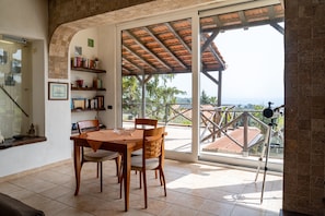 A dining area with a table and chairs, a bookshelf, and a balcony with a telescope. - Villa "In the Green" of Etna with Sea View, Pool, Wi-Fi, Terrace & Garden (piedimonte etneo)