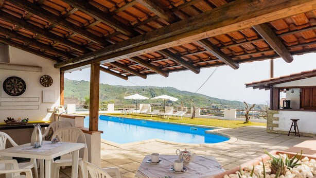A covered outdoor area with a pool, white chairs, and a table with a teapot. - Villa "Nel Verde" dell'Etna with Sea View, Pool, Wi-Fi, Terrace and Garden (piedimonte etneo)