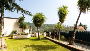 A well-maintained garden with palm trees, a white building, and a view of hills in the background. - Villa "Nel Verde" dell'Etna with Sea View, Pool, Wi-Fi, Terrace and Garden (piedimonte etneo)