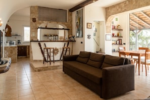 A cozy living area with a sofa, a dining table, and a kitchen with a stone wall and wooden beams. - Villa "In the Green" of Etna with Sea View, Pool, Wi-Fi, Terrace & Garden (piedimonte etneo)