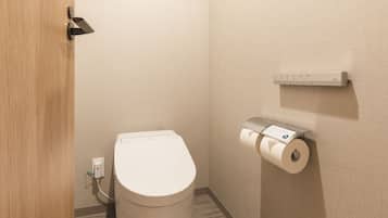 A small, modern bathroom with a toilet, a paper towel dispenser, and a wall-mounted electrical outlet.