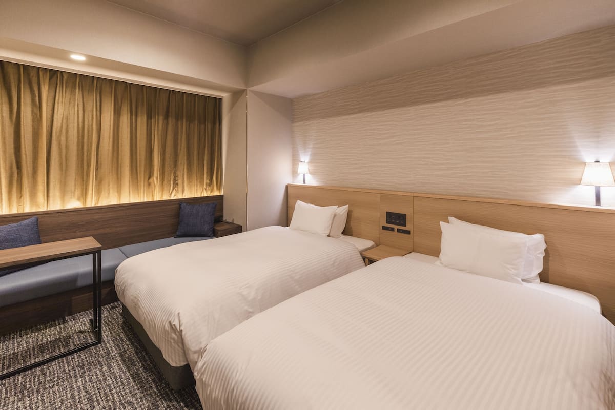 Una habitación de hotel con dos camas, un escritorio y una ventana con cortinas.