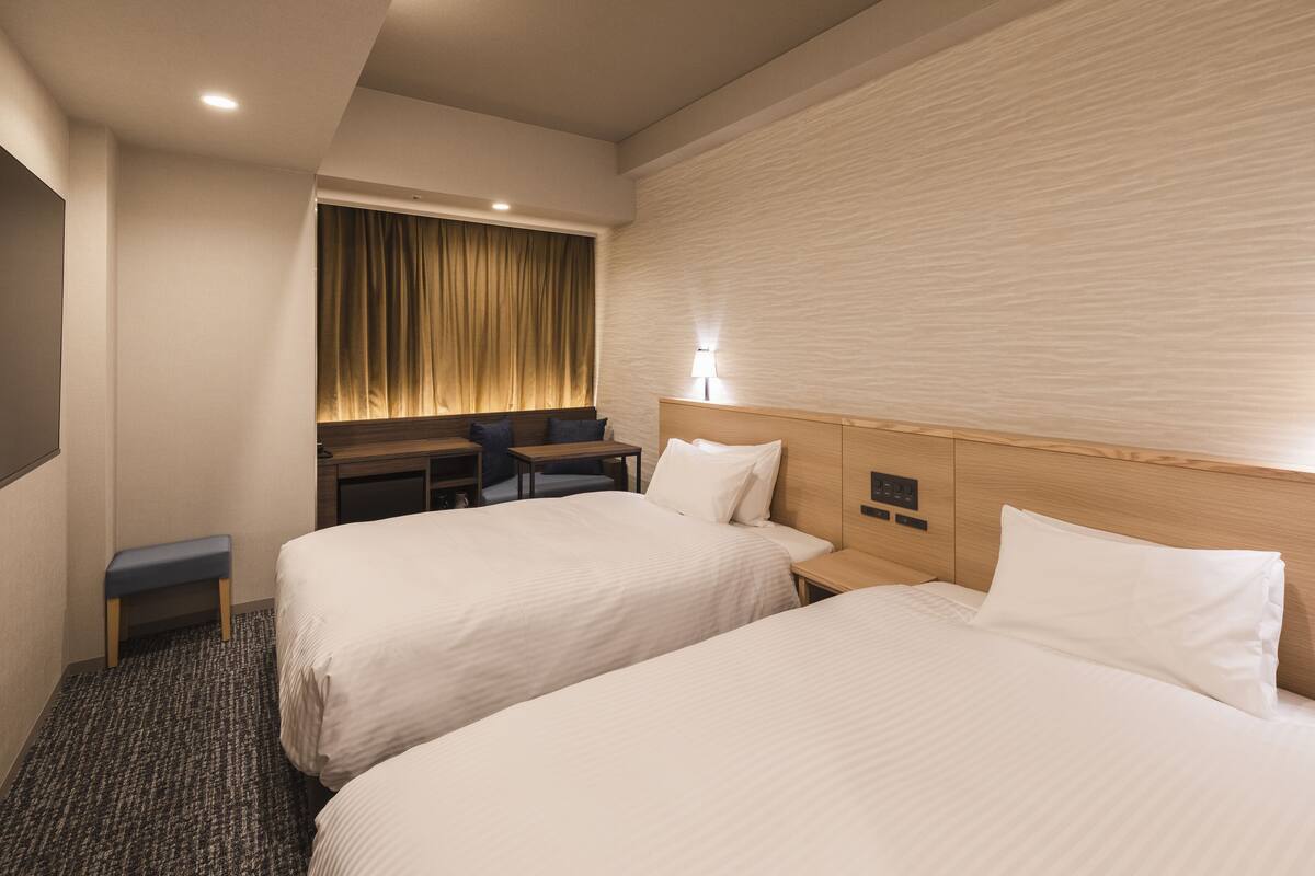 Habitación de hotel con dos camas, un escritorio, una silla y un pequeño banco.