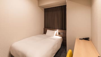 Una habitación de hotel con una cama individual, cabecera de madera, un escritorio y una silla.