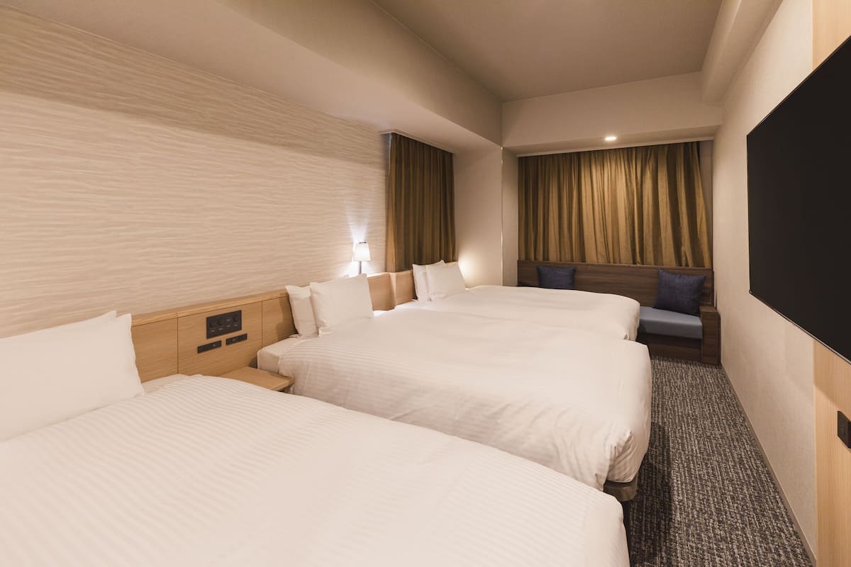 Habitación de hotel con tres camas, televisión, escritorio y zona de estar con cortinas.