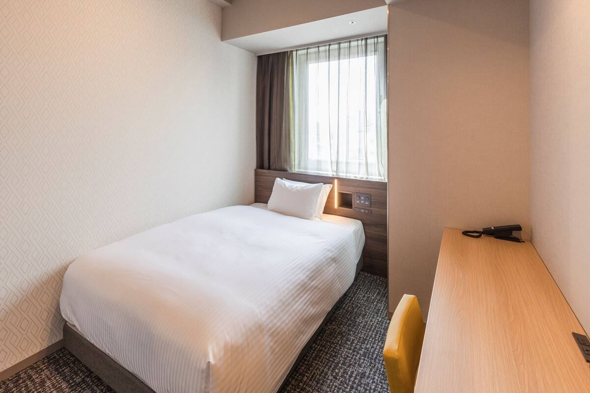 Una habitación de hotel con una cama individual, un escritorio y una ventana con cortinas.