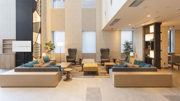 A spacious lobby with a central seating area, two armchairs, a sofa, and a coffee table. There are two side tables with lamps, a potted plant, and a sign that reads "GRAND FRÈS." - SOTETSU GRAND FRESA TAKADANOBABA (Tokyo)