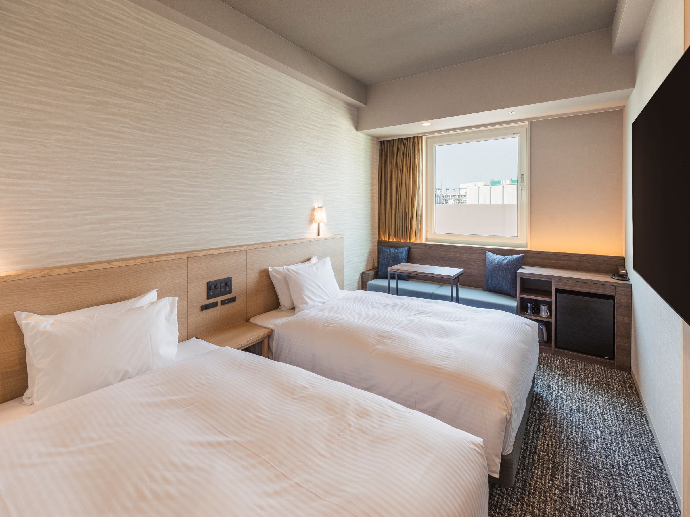 A hotel room with two beds, a desk, a chair, a window with curtains, and a television.