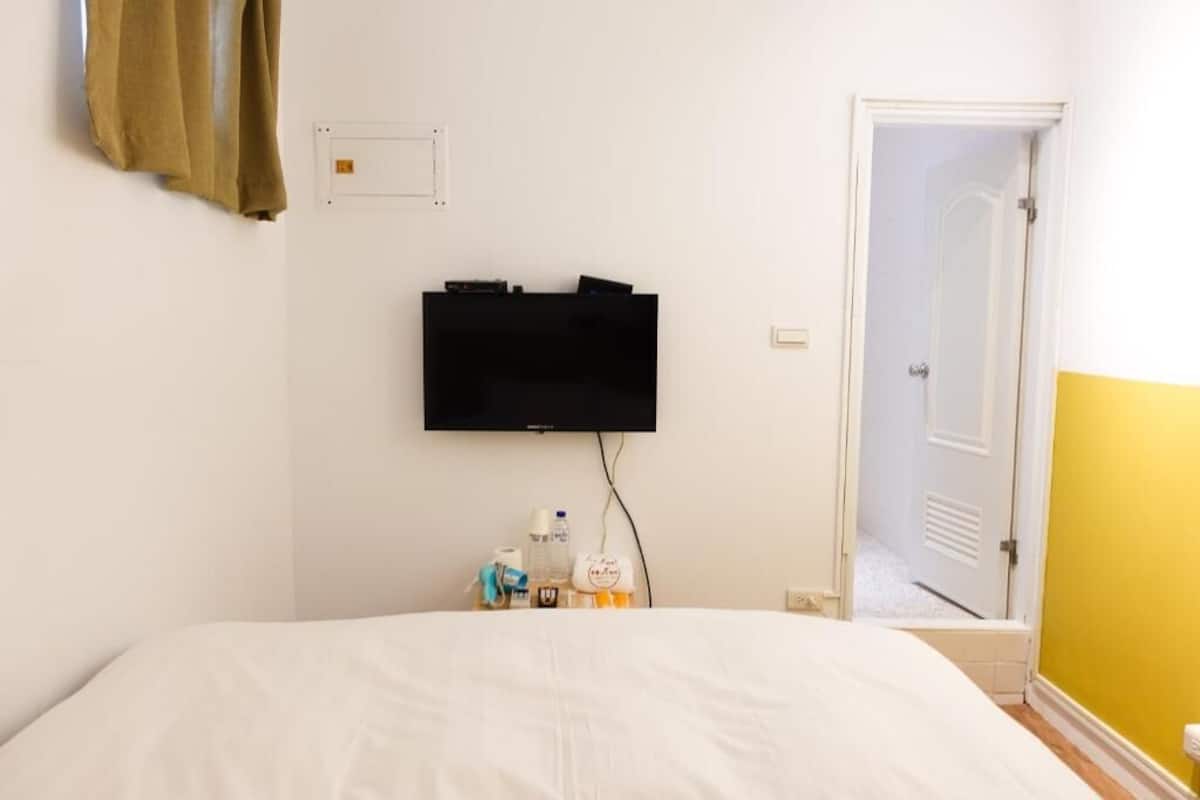 Une chambre d’hôtel avec un lit, un téléviseur fixé au mur et une porte donnant sur un couloir.