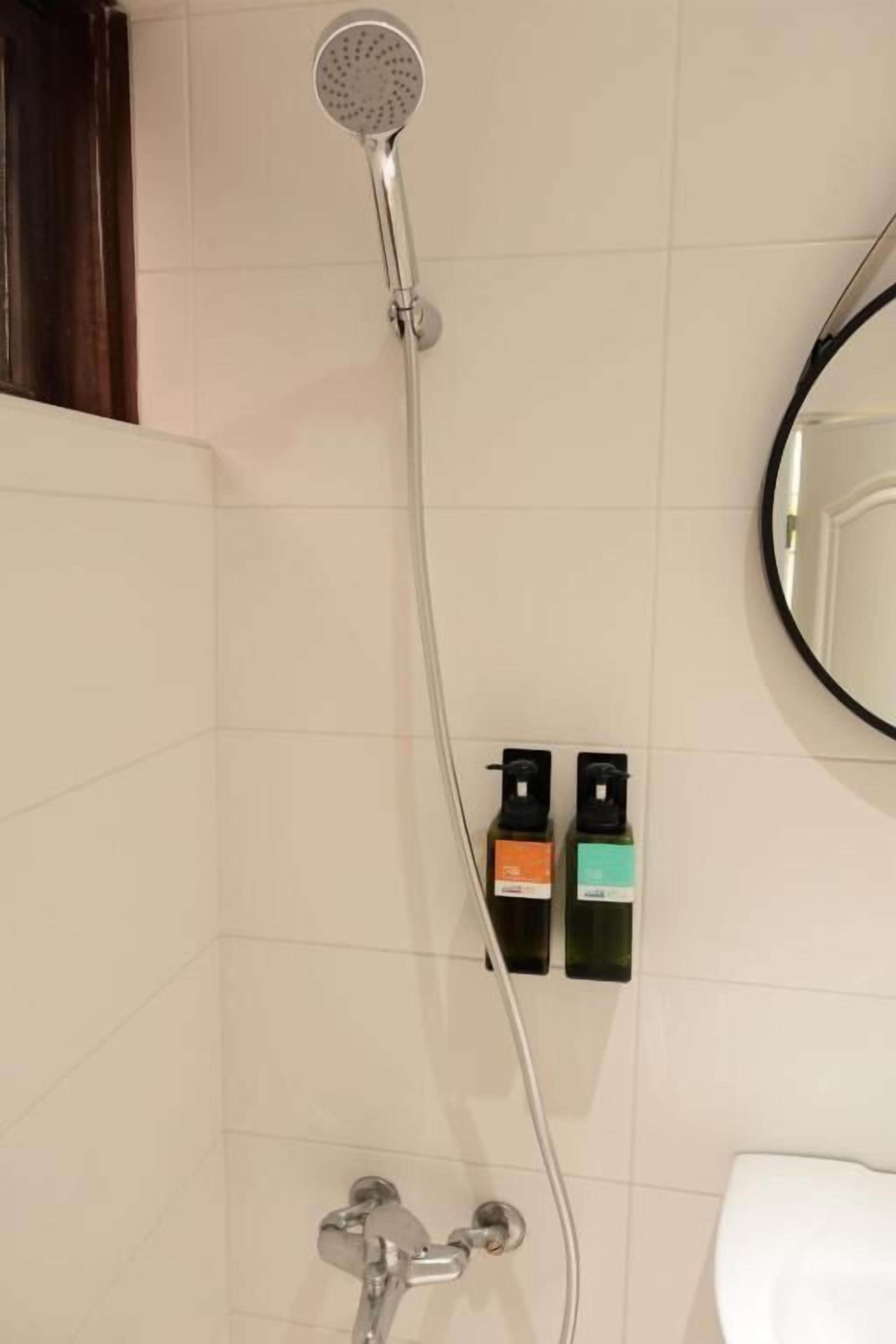 A shower with a handheld showerhead, a wall-mounted control panel, and a toilet.