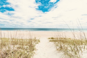 A beach path leading to the ocean with sand and grass on either side.