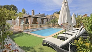 A swimming pool with lounge chairs and umbrellas, surrounded by a garden and a building with a tiled roof. - Llimona - Cozy house with pool in Alcúdia, Mallorca (Alcúdia)