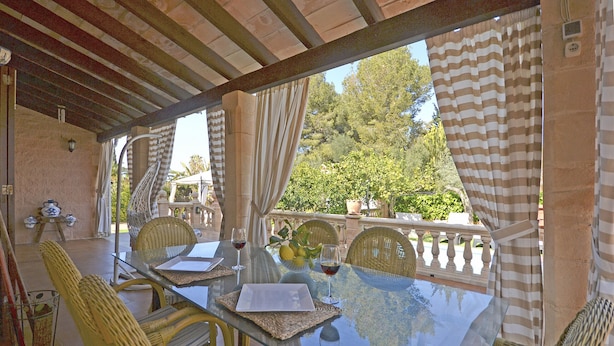 An outdoor dining area with a glass table, wicker chairs, and striped curtains. - Llimona - Cozy house with pool in Alcúdia, Mallorca (Alcúdia)