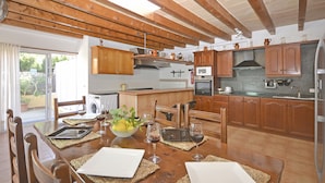A kitchen with wooden cabinets, a dining table set for four, and a view of the outdoors. - Llimona - Cozy house with pool in Alcúdia, Mallorca (Alcúdia)